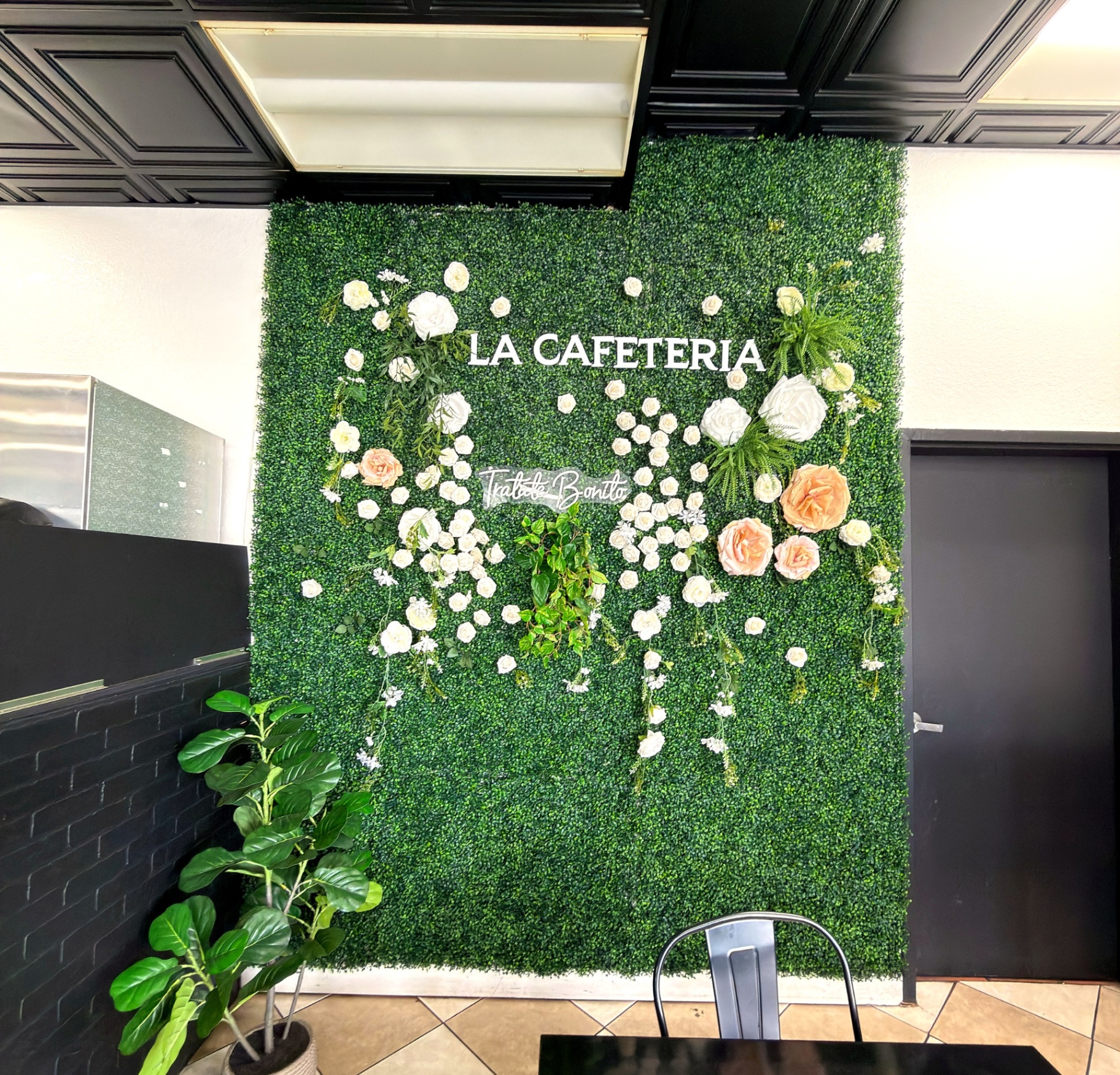 La Cafeteria greenery and flower wall with 'Trátate Bonito' neon sign