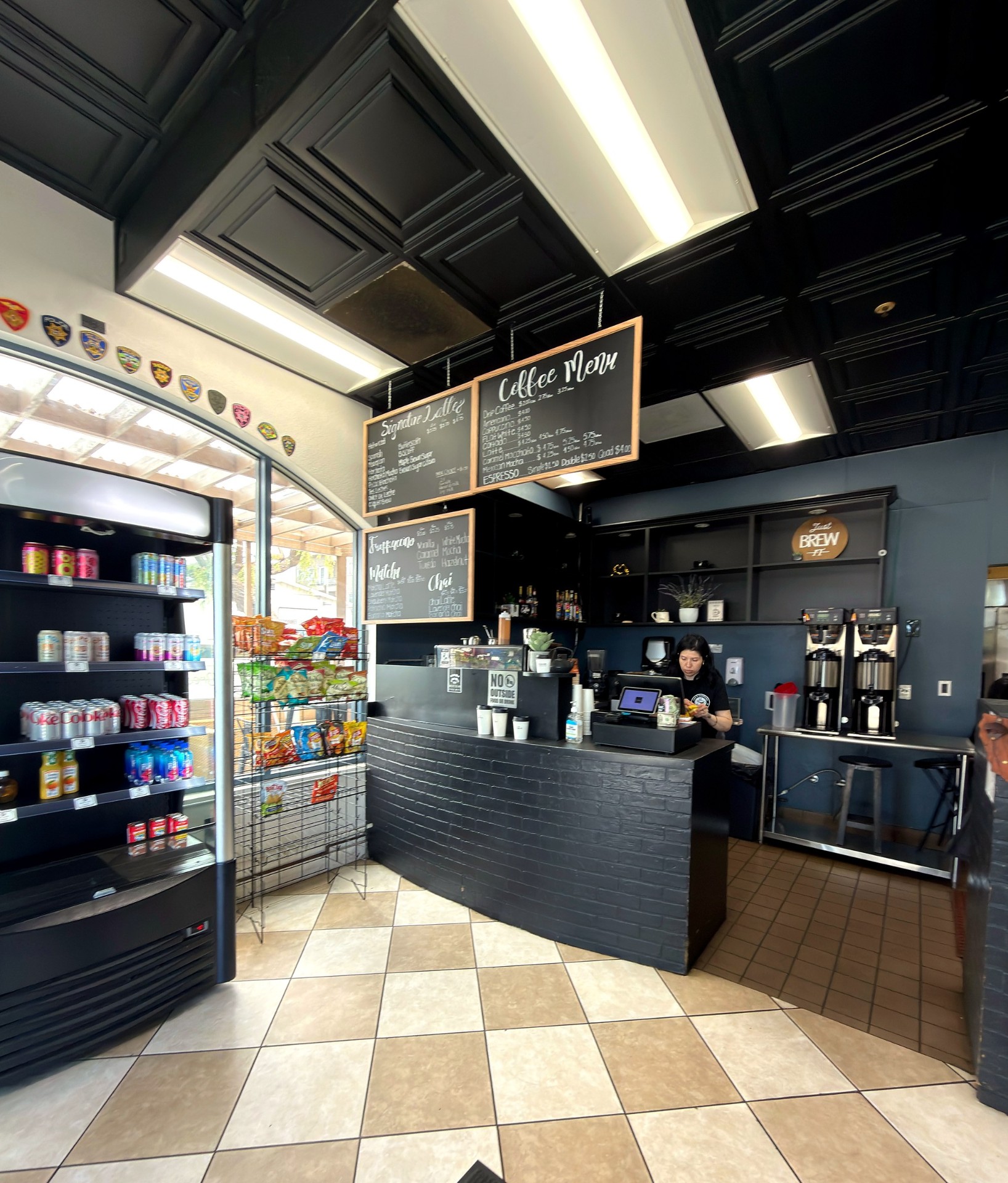 Barista behind the counter at La Cafeteria with chalkboard coffee menu overhead