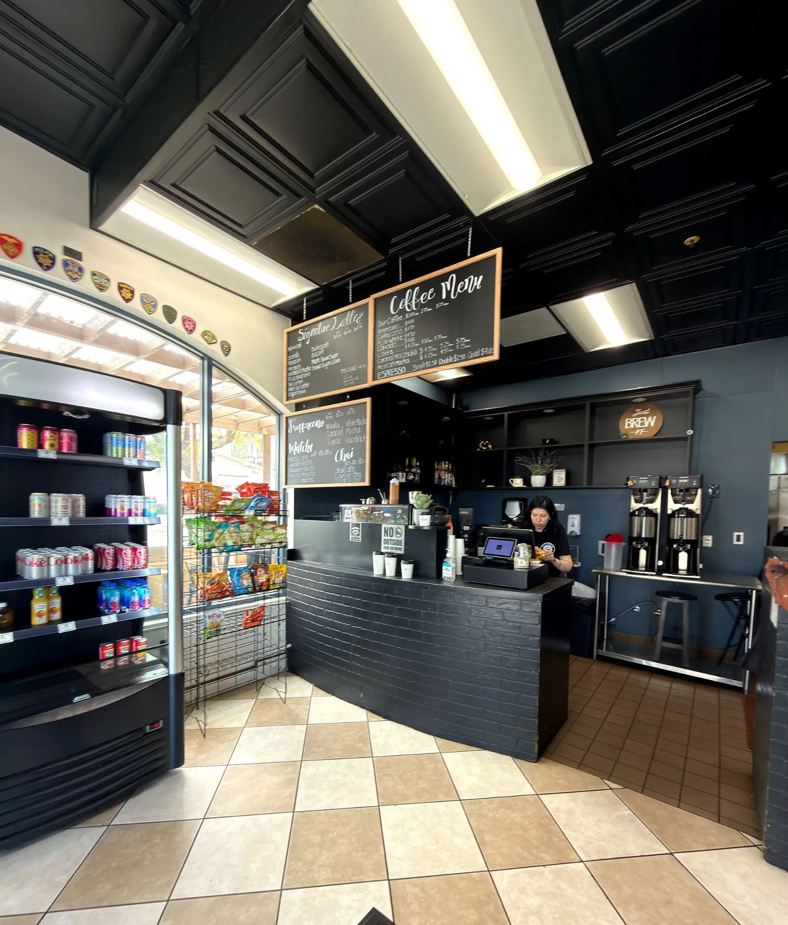 Barista behind the counter at La Cafeteria with chalkboard coffee menu overhead